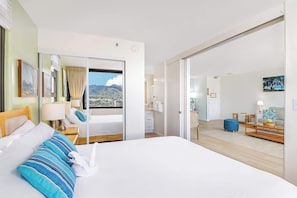 Habitación de hotel con cama, escritorio, silla, ventana con vistas y puerta corredera que da a un balcón.