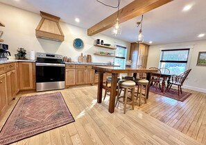A kitchen with wooden cabinets, a stainless steel oven, a wooden island with stools, and pendant lighting. - Our Guest House (State College)