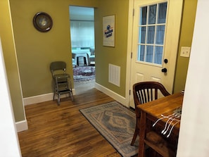 A hallway with a wooden floor, a door with a window, a chair, and a rug. - Our Guest House (State College)