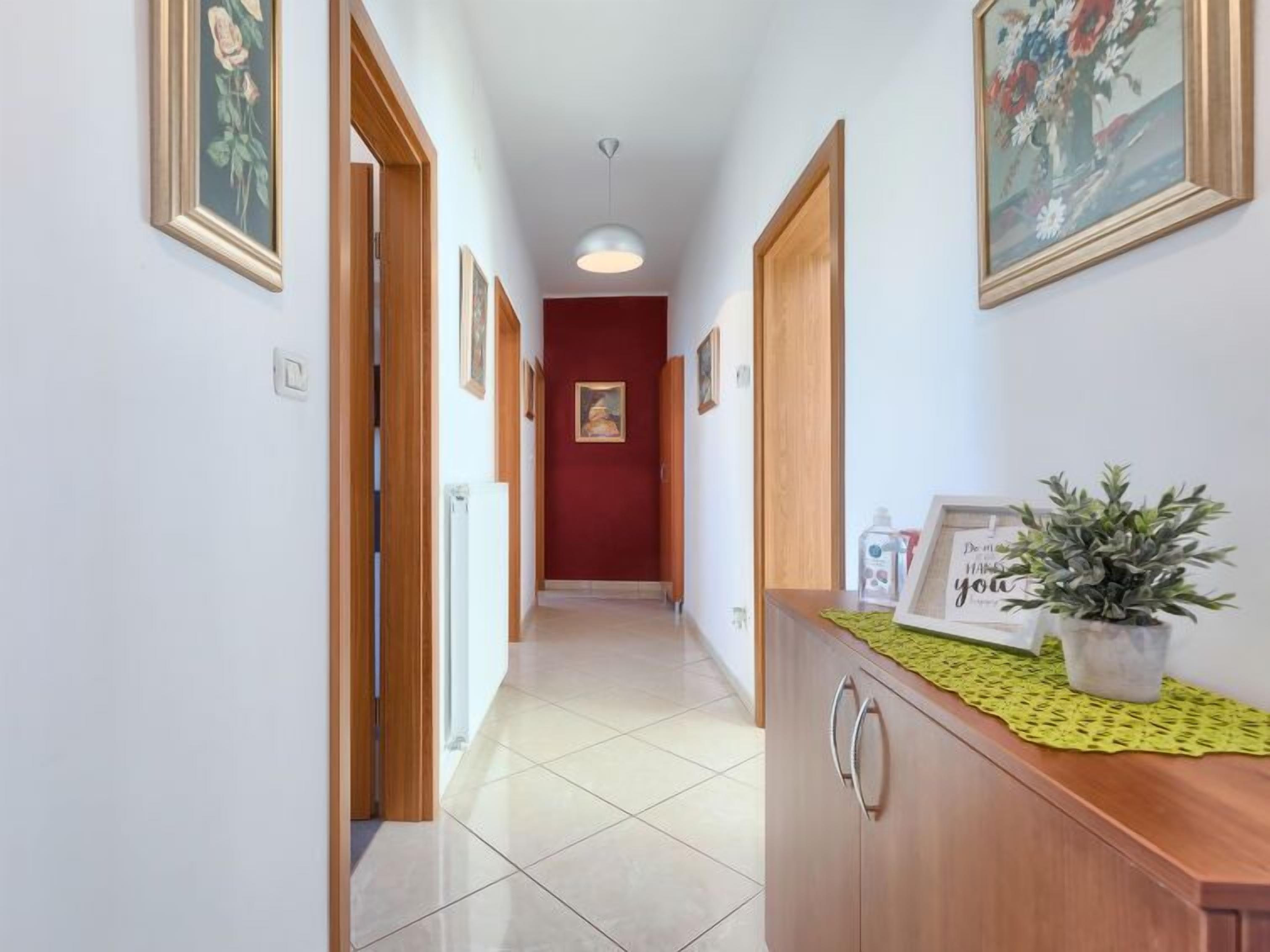 A hallway with a wooden cabinet, framed artwork, and a potted plant.