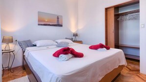 A hotel room with a bed, two pillows, a nightstand, a lamp, a painting of a lighthouse, and a wooden wardrobe. - Apartment Laura by Interhome (Pula/Galižana)