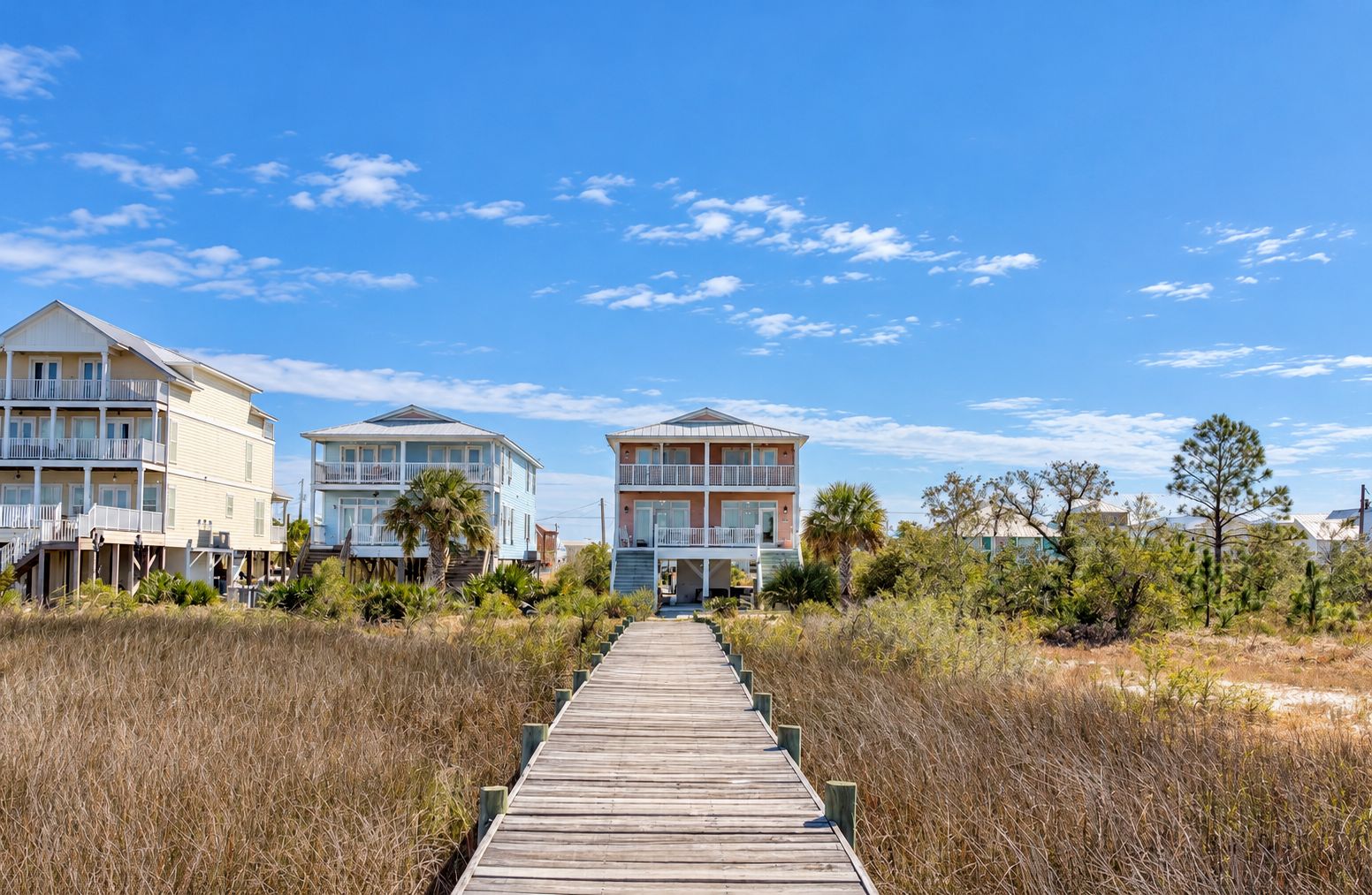 A wooden boardwalk leading to beachfront properties with multiple stories and balconies.