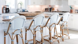 Una cocina moderna con armarios blancos, una isla grande con taburetes de bar y una decoración original de pez.