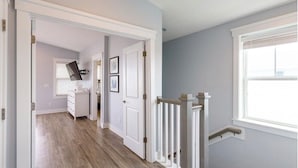 Un pasillo con piso de madera, paredes blancas y una puerta blanca que da a otra habitación.
