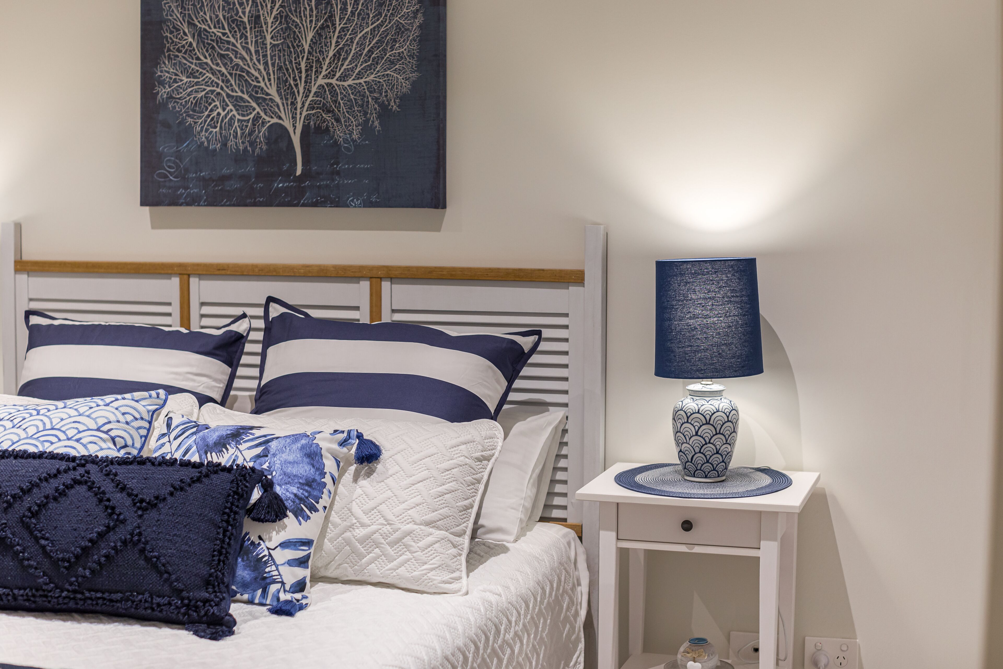 A neatly made bed with striped bedding, a bedside table with a lamp, and a wall-mounted artwork.