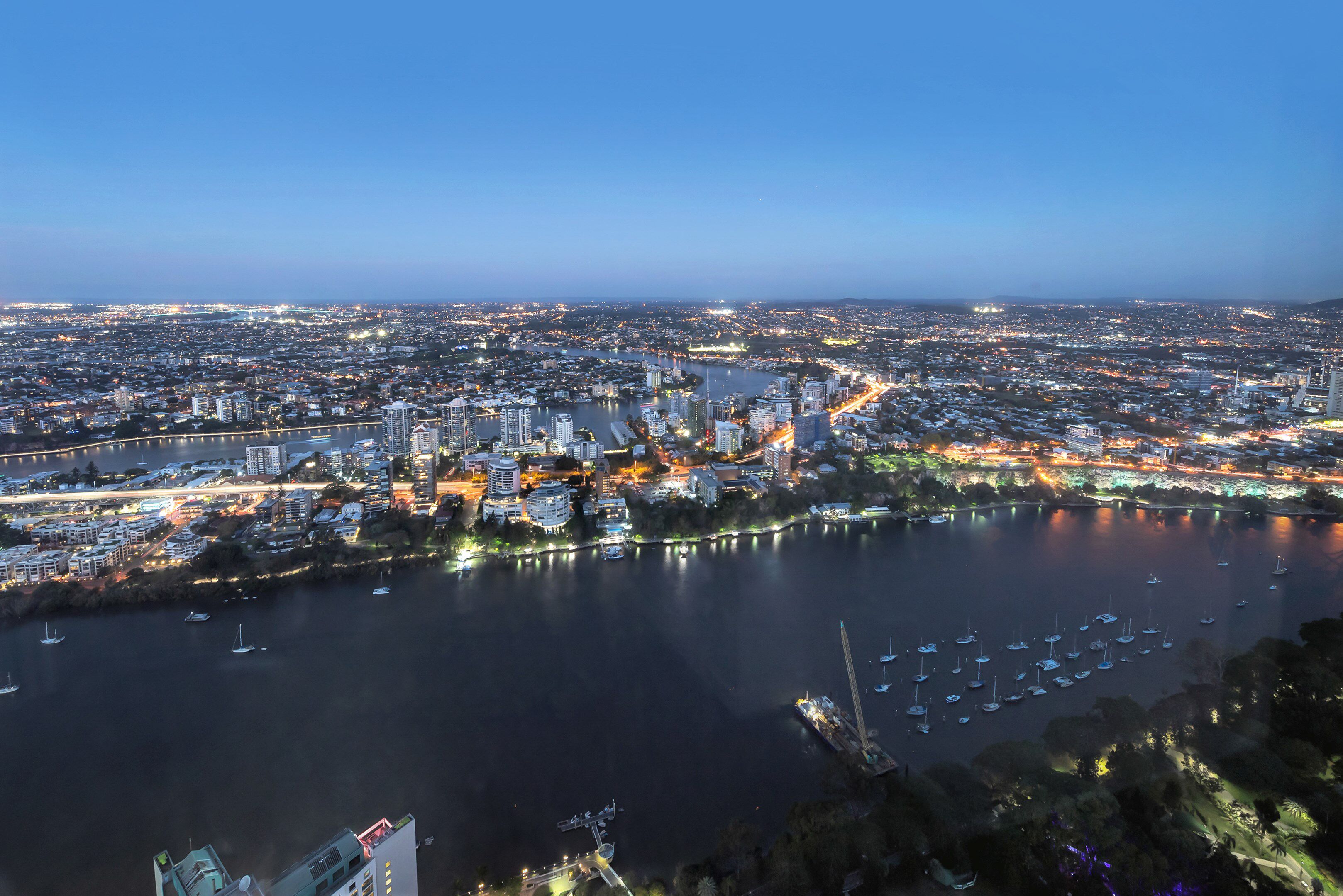 Vista panorámica de un paisaje urbano al atardecer, con un río y un puerto deportivo.