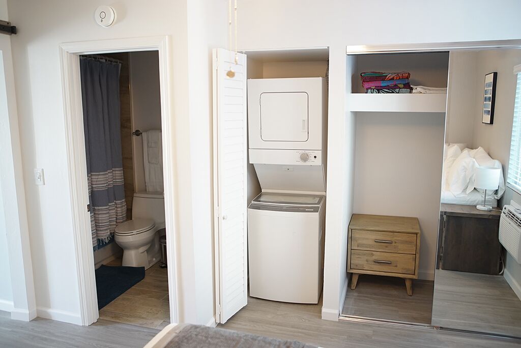 A compact room with a built-in washer and dryer, a small wooden nightstand, and a closet with hanging space.