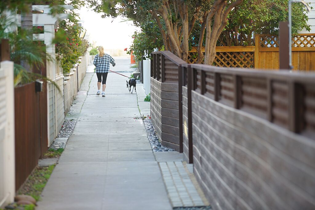 A narrow sidewalk with a wooden fence on one side and a metal fence on the other.
