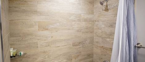 Un espace douche avec des murs recouverts de carreaux beiges et un pommeau de douche.