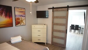 Ein Schlafzimmer mit einem Bett, einer Kommode, einem Fernseher und einer Schiebetür, die auf einen Balkon führt.