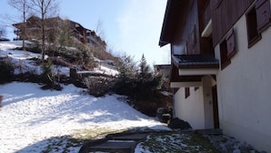 A snow-covered pathway leading to a building with a wooden facade and a balcony.