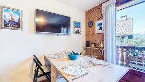 A dining area with a table set for four, a television above, and a view of a house and landscape through a window.