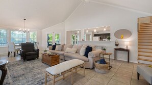 A spacious living room with a high ceiling, a large window, a ceiling fan, and a cozy seating area with a sofa, armchair, and ottoman. - Lake It Easy...5BR Waterfront Home, Dock, Deck and Game Area (New Braunfels)