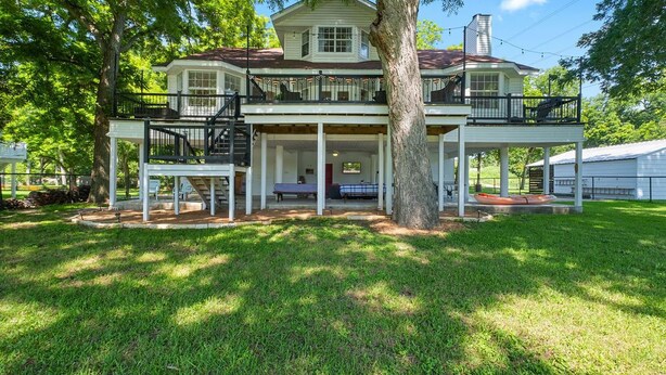 A two-story house with a porch, a covered front porch area, and a staircase leading to the upper level. - Lake It Easy...5BR Waterfront Home, Dock, Deck and Game Area (New Braunfels)