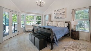 A spacious bedroom with a large bed, a bench, and a chandelier. - Lake It Easy...5BR Waterfront Home, Dock, Deck and Game Area (New Braunfels)