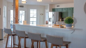 A kitchen with a white island, green cabinets, and three wicker bar stools. - Lake It Easy...5BR Waterfront Home, Dock, Deck and Game Area (New Braunfels)