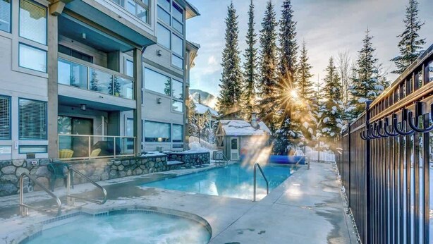 A hotel with a pool, outdoor seating, and a view of snow-covered trees. - Greystone Lodge 328 Ski-in/Out by Acer Vacations (Whistler)