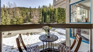 A balcony with a table, chairs, and a view of a snowy landscape with trees. - Greystone Lodge 328 Ski-in/Out by Acer Vacations (Whistler)