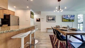 A modern kitchen with a bar area, dining table with chairs, and a chandelier. - Greystone Lodge 328 Ski-in/Out by Acer Vacations (Whistler)