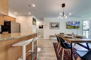A modern kitchen with a bar area, dining table with chairs, and a chandelier.
