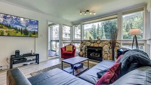 A modern living room with a stone fireplace, large windows, a red armchair, and a black coffee table. - Greystone Lodge 328 Ski-in/Out by Acer Vacations (Whistler)