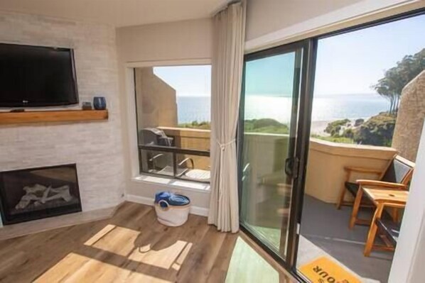 A room with a fireplace, a television, a balcony with a view of the sea, and a sliding glass door.
