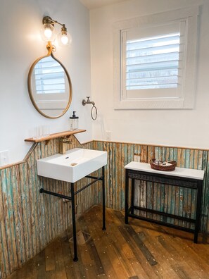 Ein Badezimmer mit einem weißen Waschbecken, einem Holzschrank und einem kleinen Tisch mit einem Korb.