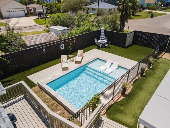 Ein Garten mit Schwimmbecken, Liegestühlen, einem kleinen Tisch und einer Terrasse.
