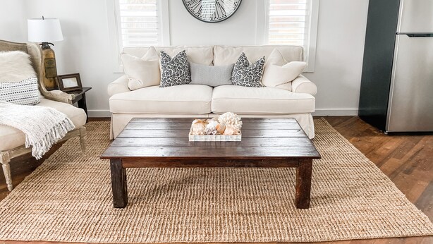 A living room with a beige sofa, a wooden coffee table, a large wall clock, and a modern refrigerator.