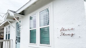 A white building with a door and windows, and a sign on the wall that says "shore thing".