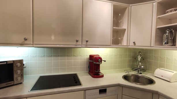 Una cocina con armarios blancos, un microondas, una cafetera roja, un lavamanos y un tostador.