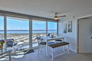 A spacious balcony with a view of the sea, a dining table with chairs, and a ceiling fan.