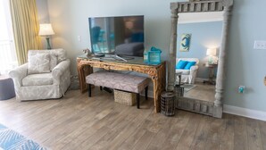 Una sala de estar con una mesa de centro de madera, un sofá blanco, un banco, un televisor y un espejo con un cartel que dice 'Beach'.