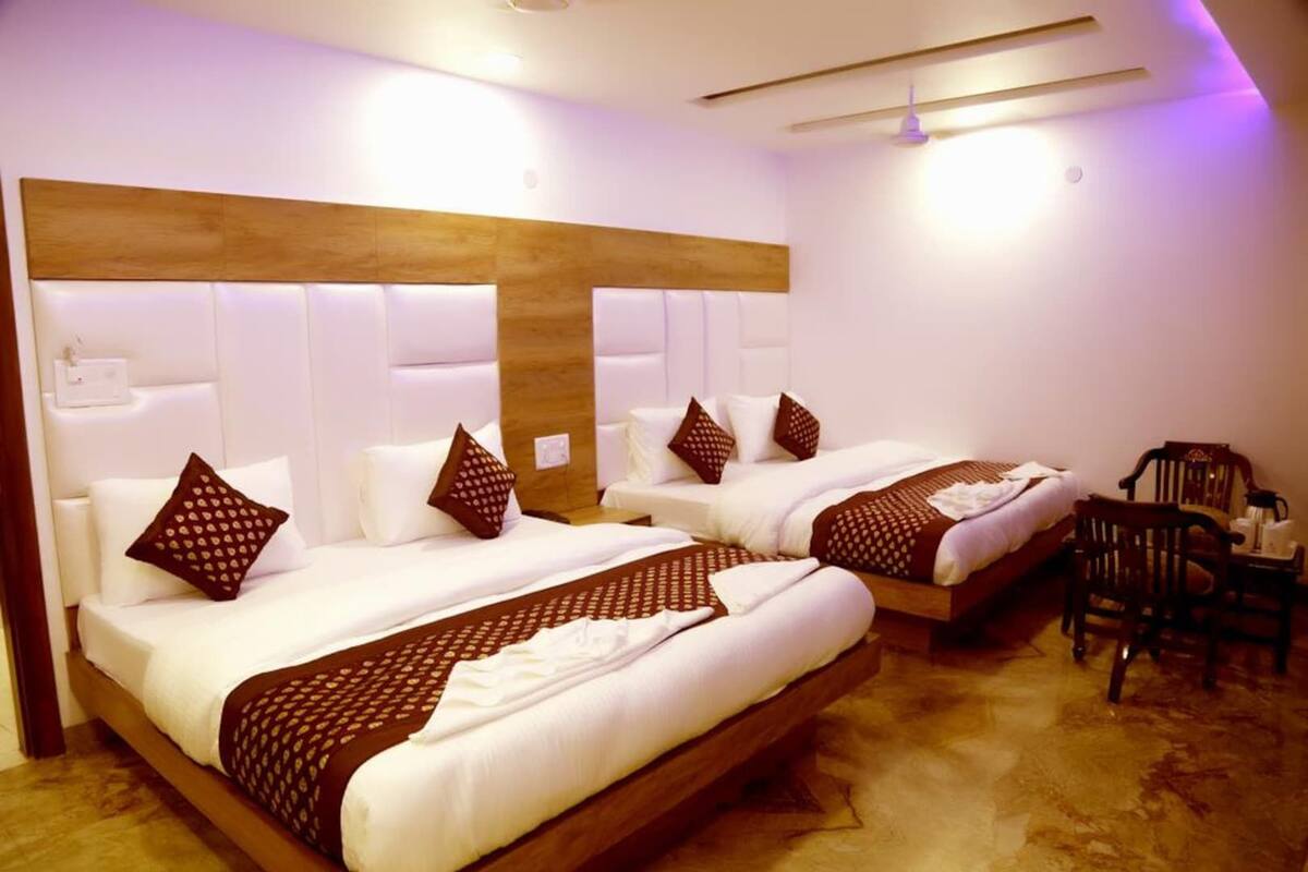 Una habitación de hotel con dos camas, cabecero de madera, ropa de cama blanca y suelo de madera.