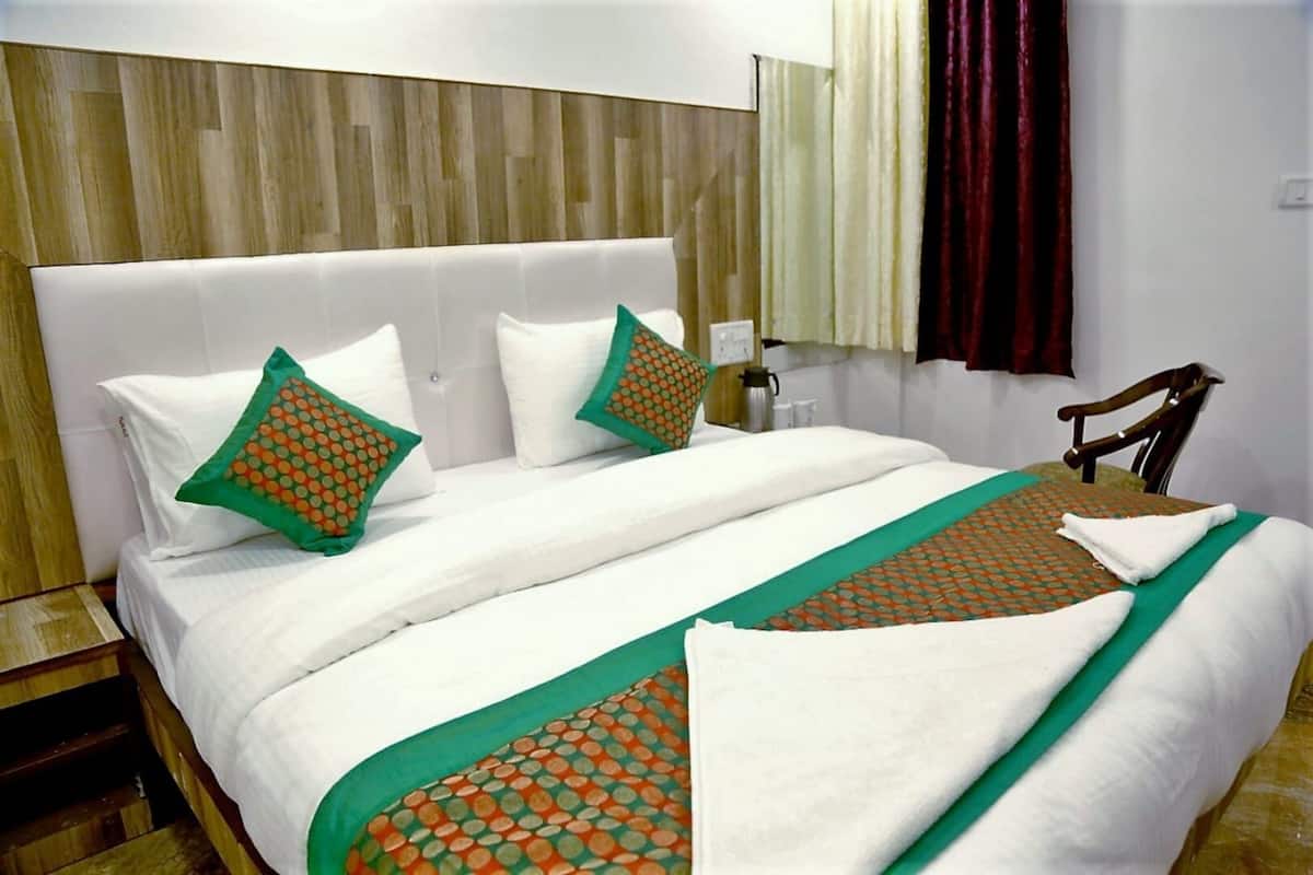 Habitación de hotel con una cama grande, dos almohadas, una mesita de noche, una silla y una ventana con cortinas.