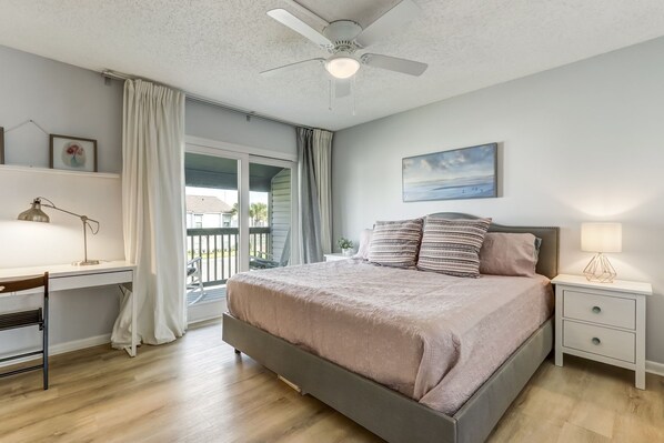 A bedroom with a bed, bedside tables, a desk, a ceiling fan, and a window with curtains.