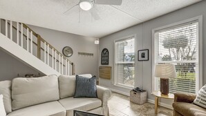 A living room with a staircase, a sofa, a lamp, and a window with blinds. - Sunny Daze - Hosted by Moore AI Rentals (Fernandina Beach)