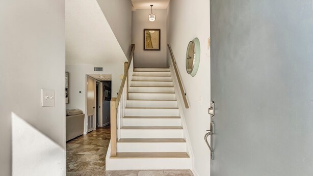 A staircase with white steps and a handrail, leading to a room with a door and a wall-mounted clock. - Sunny Daze - Hosted by Moore AI Rentals (Fernandina Beach)