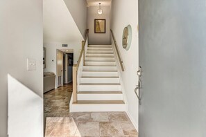 A staircase with white steps and a handrail, leading to a room with a door and a wall-mounted clock.
