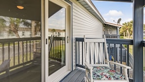 A covered porch with a sliding glass door, a small outdoor seating area with a cushioned chair, and a satellite dish on the roof. - Sunny Daze - Hosted by Moore AI Rentals (Fernandina Beach)