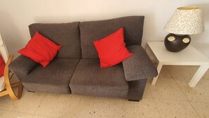 Ein graues Sofa mit zwei roten Kissen, ein weißer Sessel mit einem roten Kissen und ein kleiner weißer Tisch mit einer Lampe.