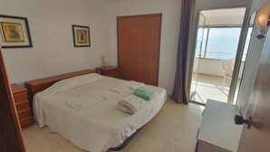 Ein Schlafzimmer mit Bett, Nachttischen, einem Kleiderschrank und Blick ins Freie.