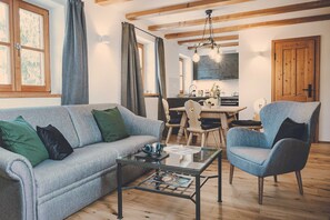 Ein Wohnzimmer mit Sofa, Sessel und Couchtisch, ein Essbereich mit Stühlen und Tisch sowie eine Küche mit Schränken und Herd.