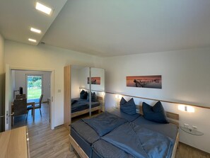 A modern bedroom with a large bed, a desk, and a chair. There is a sliding door leading to a balcony. - Spreeparadies FeWo-Semisch W3 Ranke (Märkische Heide)