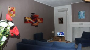 Un salon avec deux canapés bleus, un téléviseur et des œuvres d’art abstraites accrochées au mur.