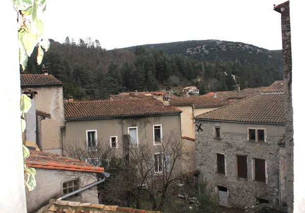 A cluster of traditional stone buildings with tiled roofs, surrounded by trees and hills in the background.
