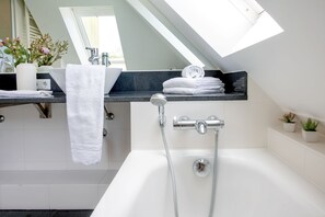 Ein modernes Badezimmer mit Dachfenster, einer Badewanne, einem Waschbecken mit Handtuch und einer kleinen Pflanze.