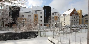 A residential area with modern buildings, a snow-covered landscape, and a metal fence.
