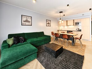 A modern living room with a green sofa, a dining area with a wooden table and chairs, and a kitchen with light wood cabinets and a microwave. - Sienkiewicz Residence (RS2.21) - RS2.21 (Swinoujscie)
