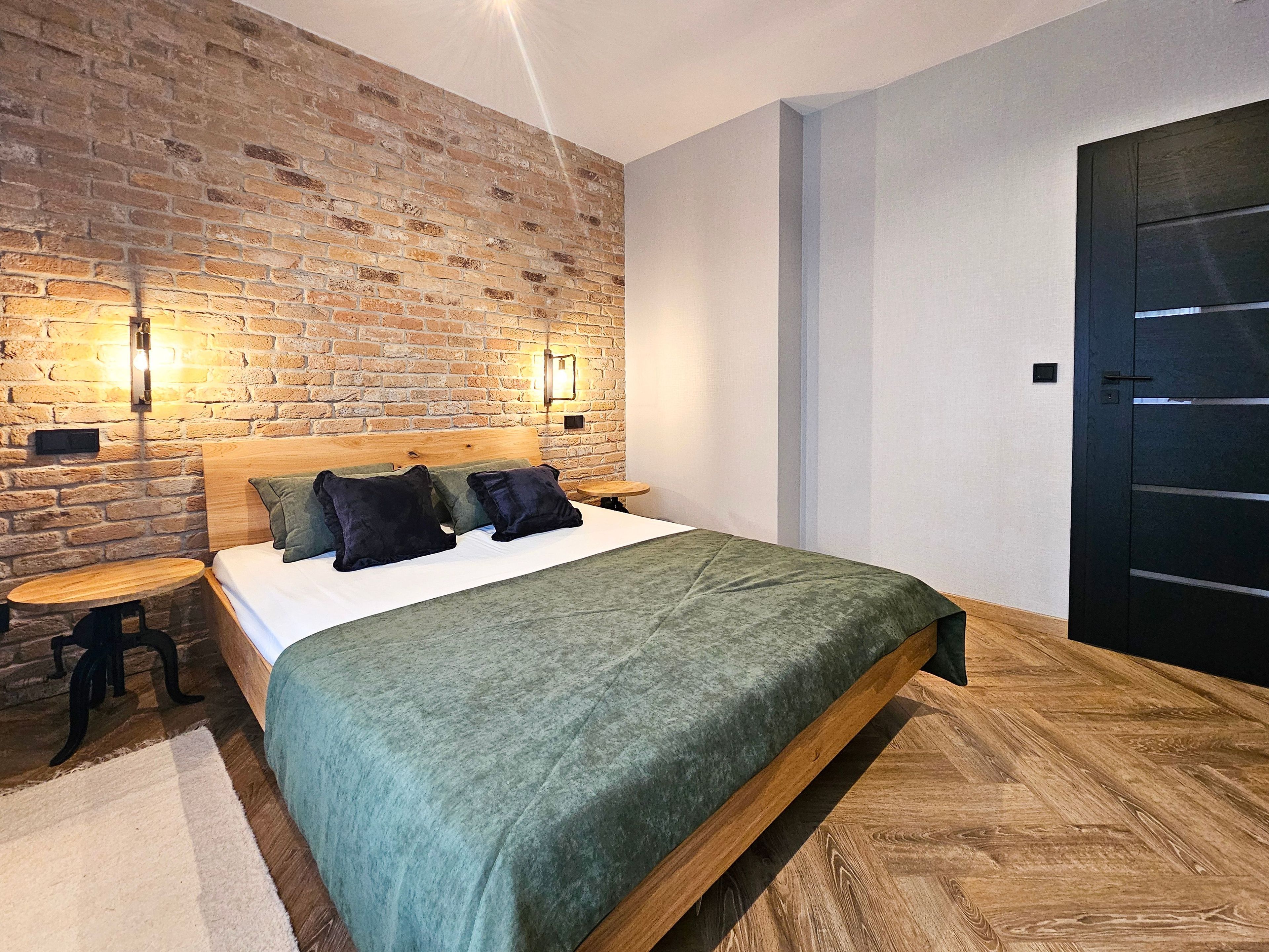 Une chambre avec un mur en briques, un cadre de lit en bois et une porte noire.